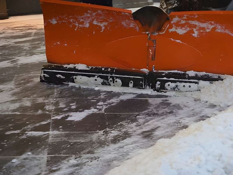 A snow plow pushing snow on pavement.