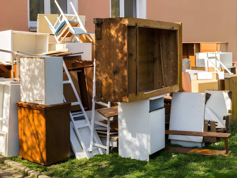 A pile of discarded wooden and white furniture outside.