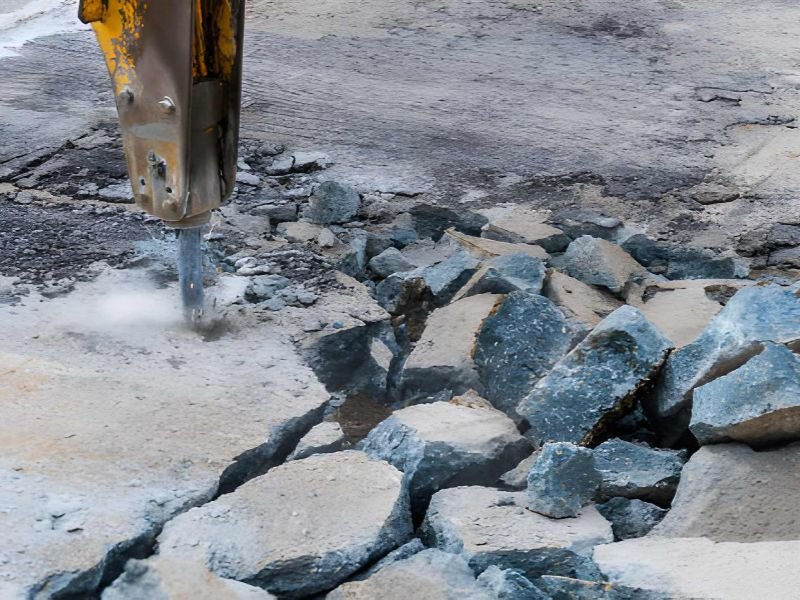 Close-up of demolition hammer with dust and sparks and broken concrete pieces