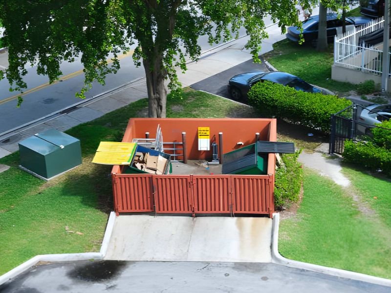 Dumpster half-filled with garbage next to residential area, road and parking lot behind commercial building