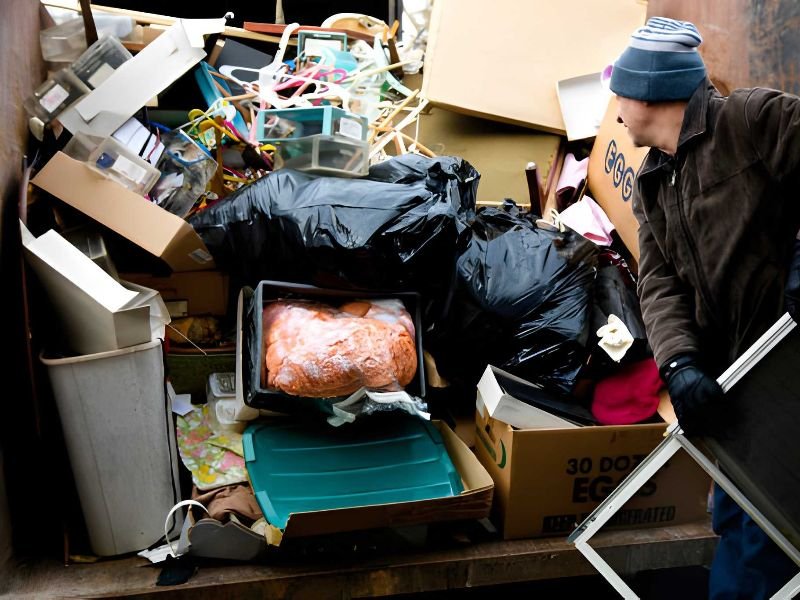 A person unloading boxes and bags into a dumpster.