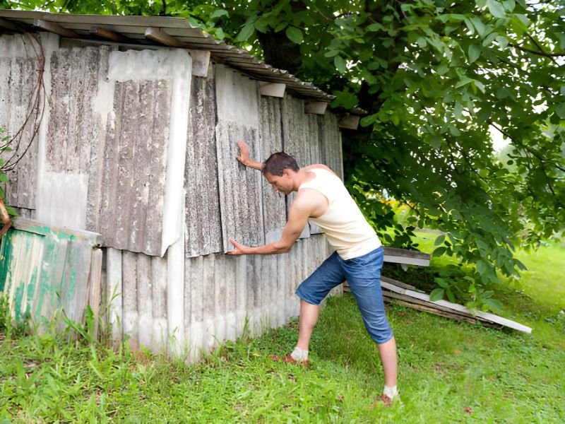 Young man farmer in garden standing fixing building shed in green summer