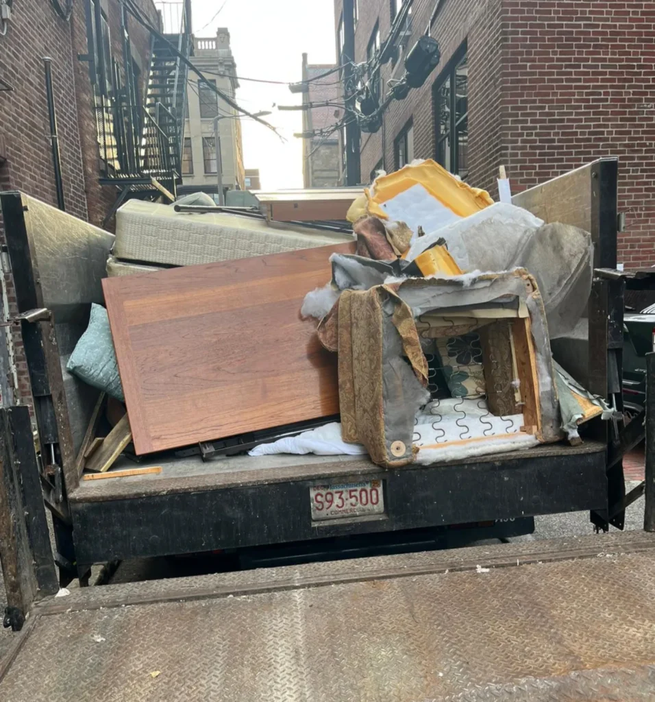 A truck bed filled with discarded furniture and debris in an alleyway